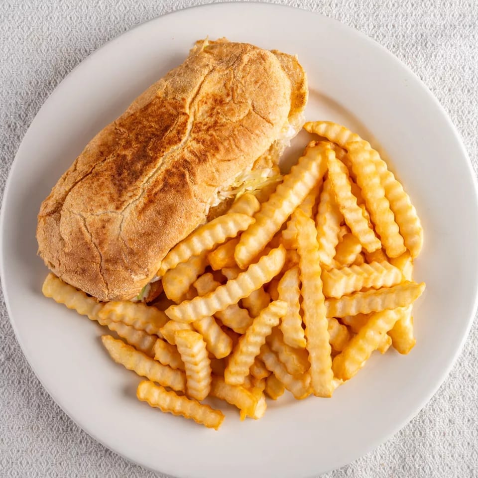 A Montecristo Taqueria y Pupuseria sandwich with crinkle-cut fries on a white plate.