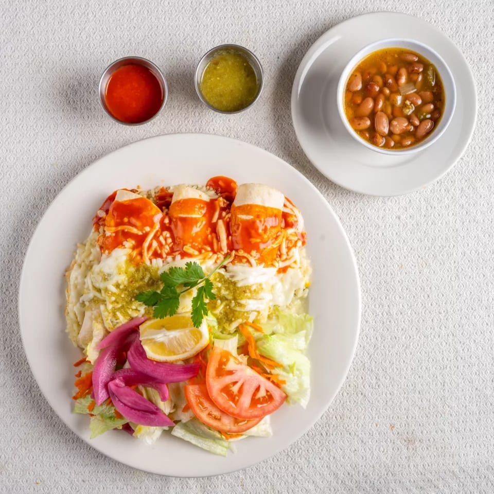 Platter of Montecristo Taqueria y Pupuseria's enchiladas with salad, beans, red and green sauces.