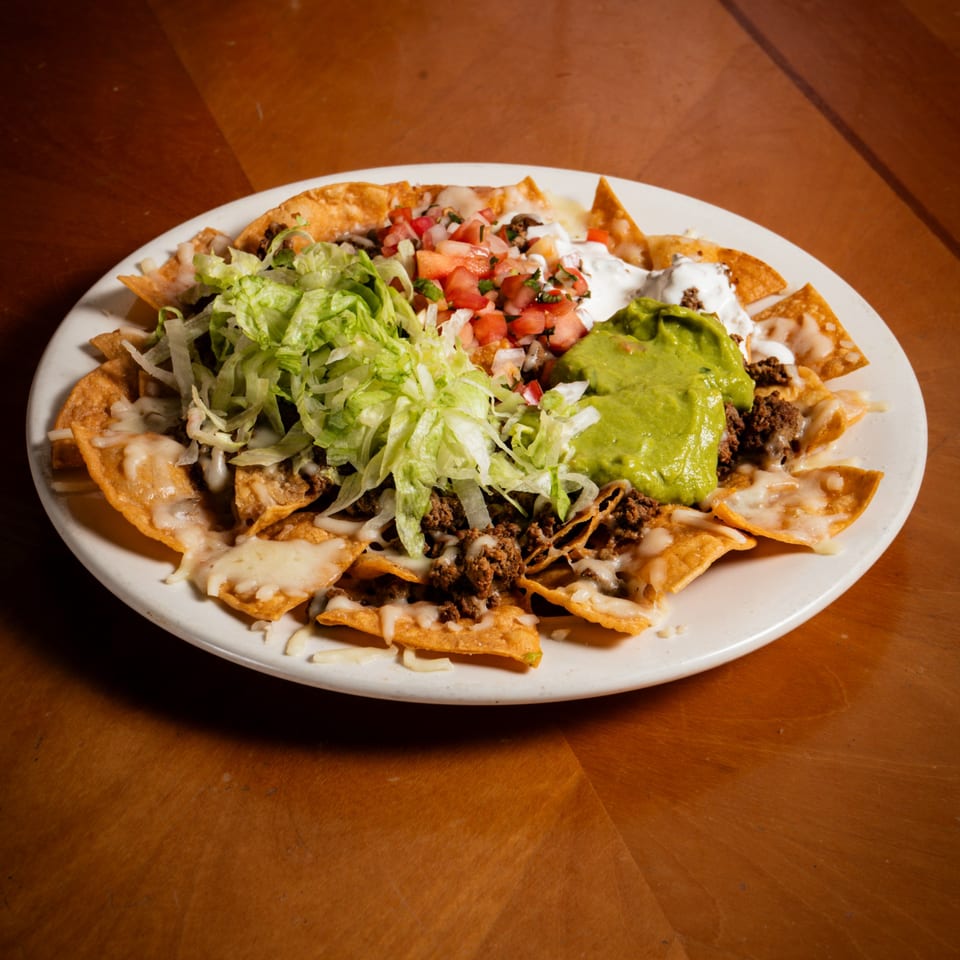 A plate of nachos with ground beef, melted cheese, shredded lettuce, pico de gallo, sour cream, and guacamole.