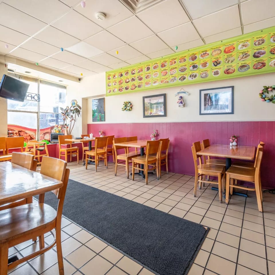 Interior of Montecristo Taqueria y Pupuseria with wooden tables and chairs, pink wainscoting, and a menu banner.